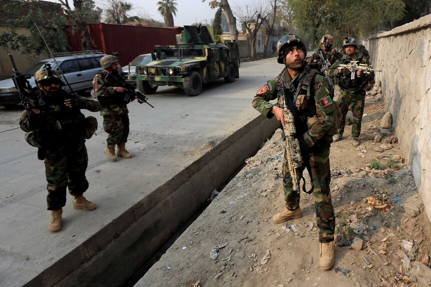 Afghan security forces holding rifles take position on the street.