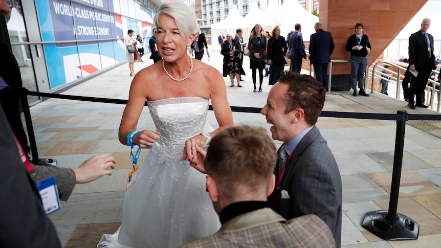 Woman with short grey hair wears wedding dress outside public building