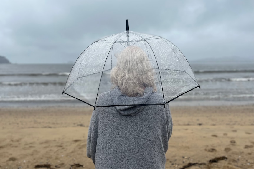 Woman with gray hair looks out on the a beach. 
