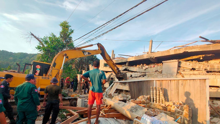 Men stand among debris in front of heavy machinery at the site of the collapse.