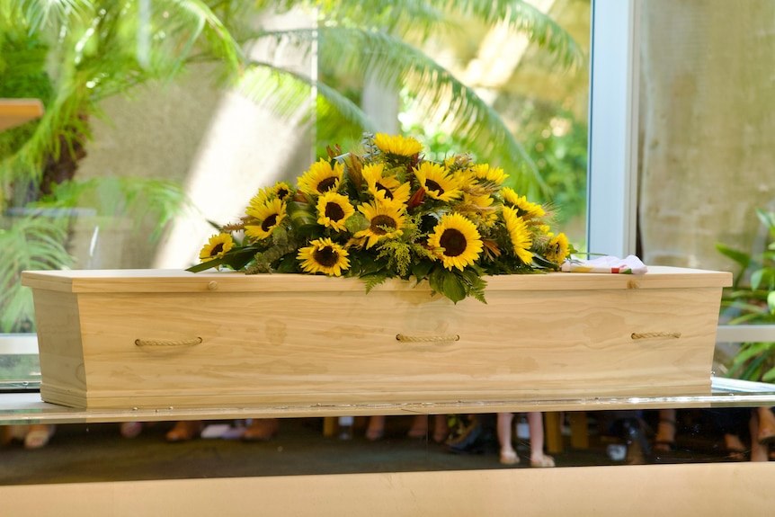 A coffin with yellow flowers on top.