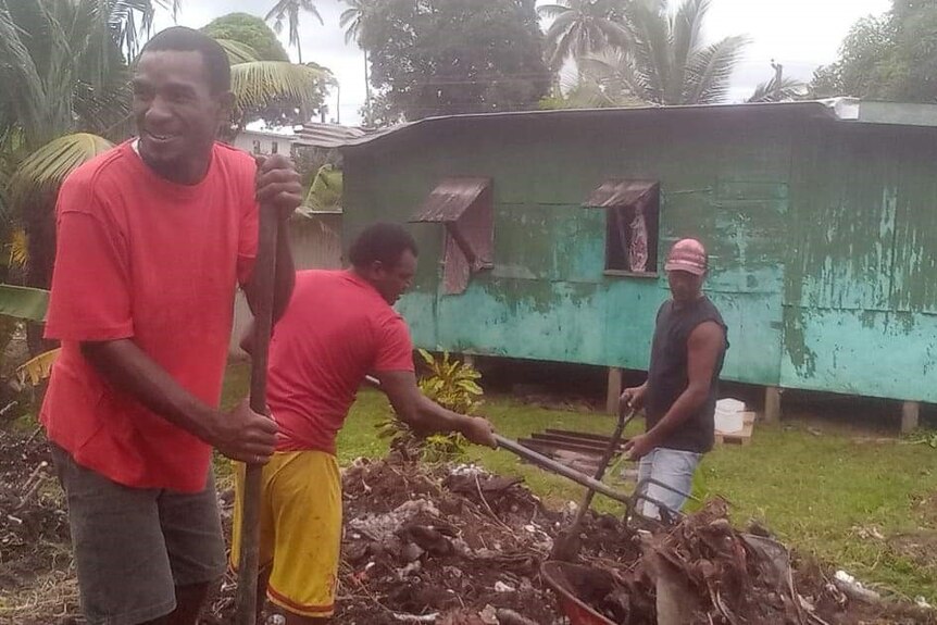Three men clean up outside their house after a cyclone. 