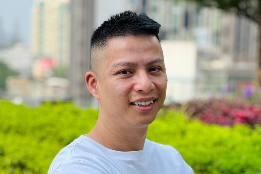 A man smiling with greenery in background.