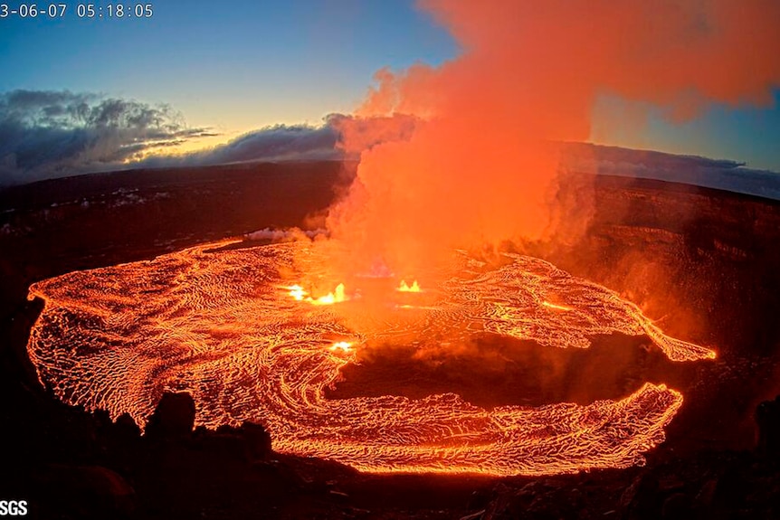 Orange smoke rising from lava in volcano crater.