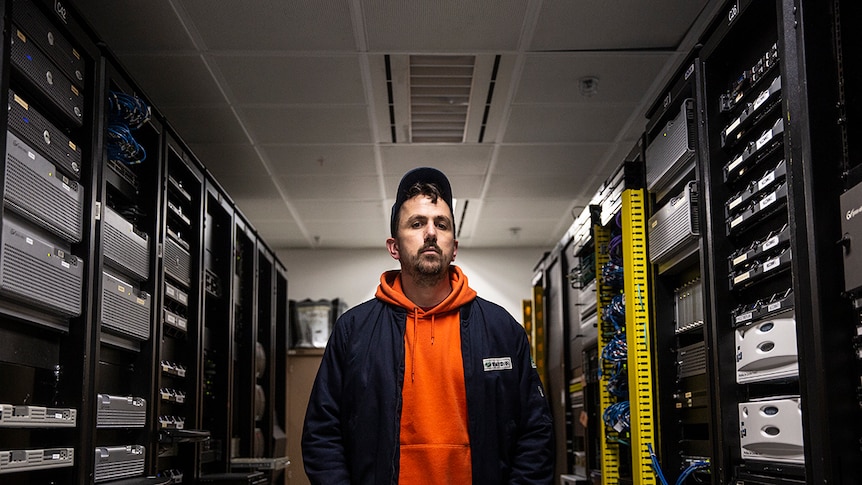 A young man stands in a room filled with computer machinery