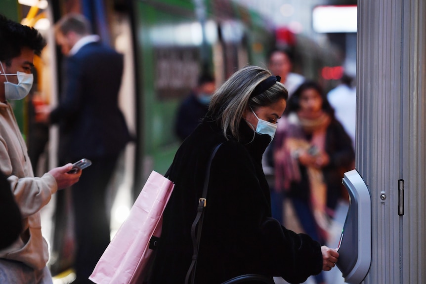 A woman wearing a medical face mask and carrying shopping bags taps off her travel card.