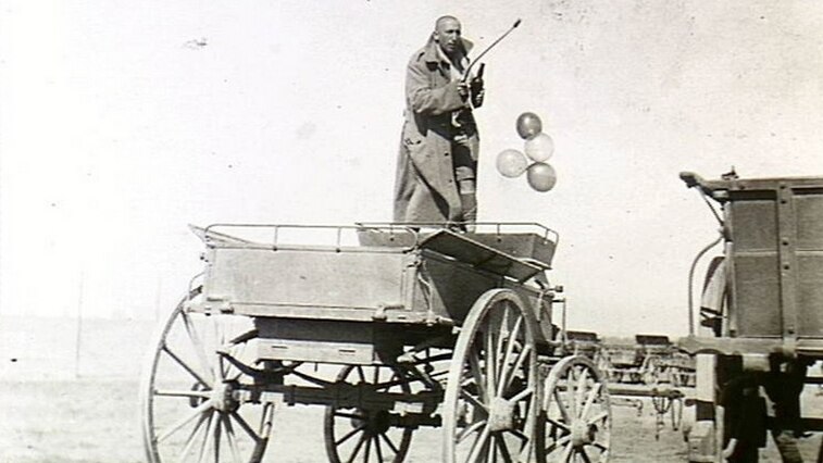 WWI soldier standing on a cart with balloons and a bottle