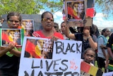 A First Nations woman stands alongside other protesters, holding a sign that reads "Black lives matter".