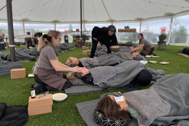 A group of women laying on the ground receiving head massages and sound therapy.  