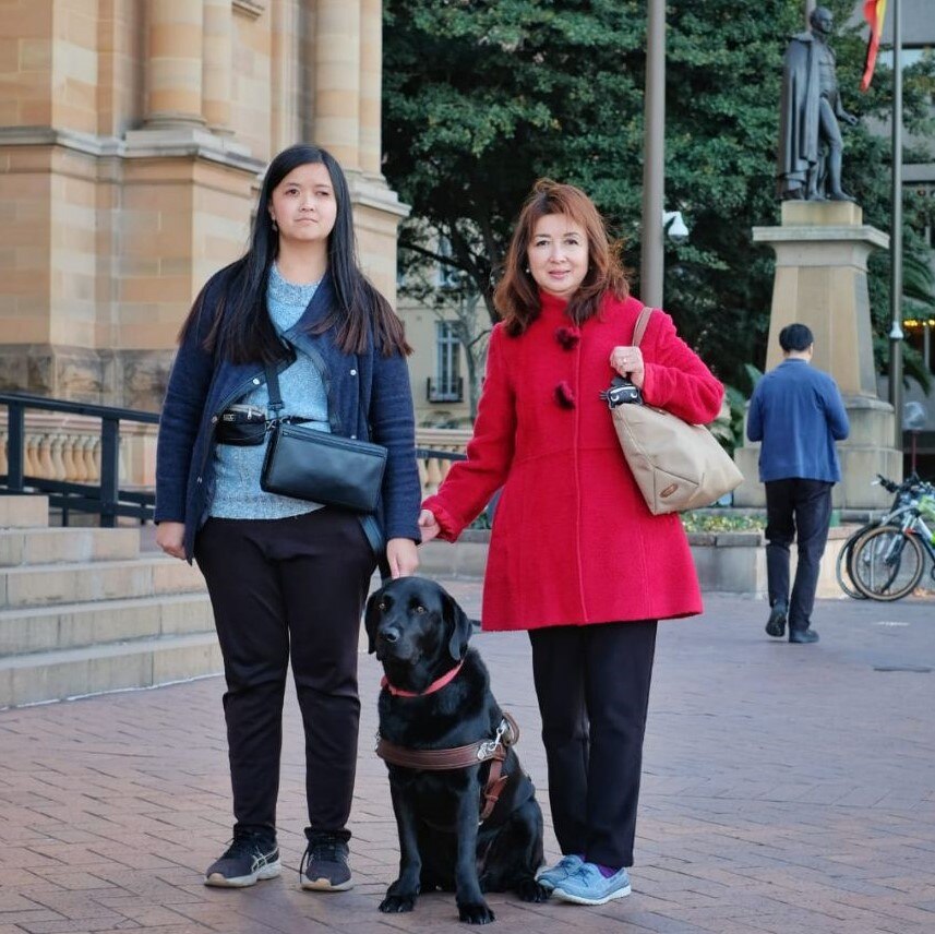 Dua orang perempuan dengan seekor anjing berdiri di depan sebuah gedung.