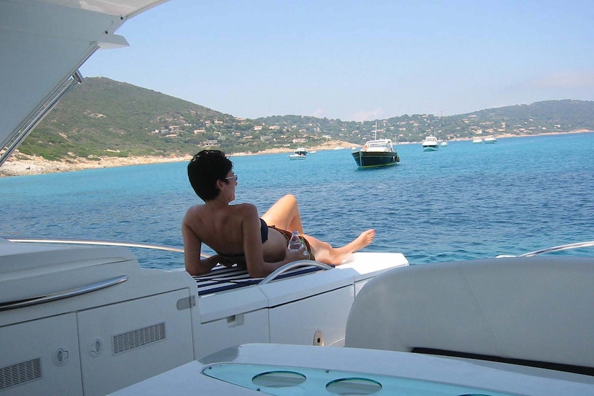 A woman reclining on a yacht docked near a beach 