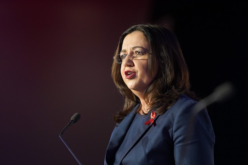 A woman with glasses speaks in front of a microphone.