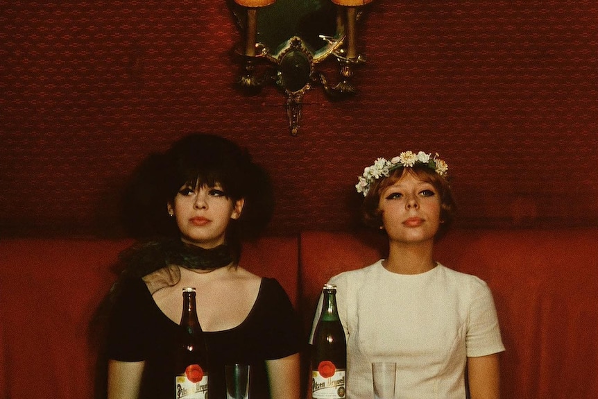 Colour still from 1966 film Daisies of Jitka Cerhová and Ivana Karbanová sitting at a small dining table with beverages.