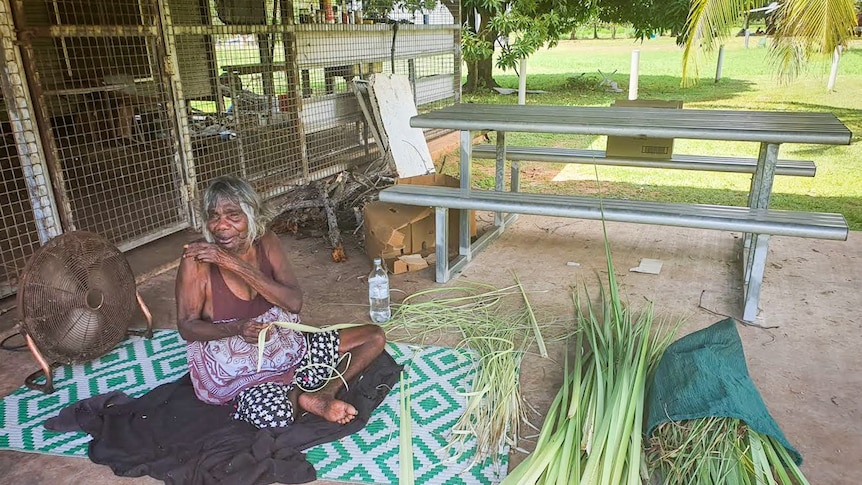 Mary Dadbalag sitting on a mat with a pile of pandanus leaves weaving.