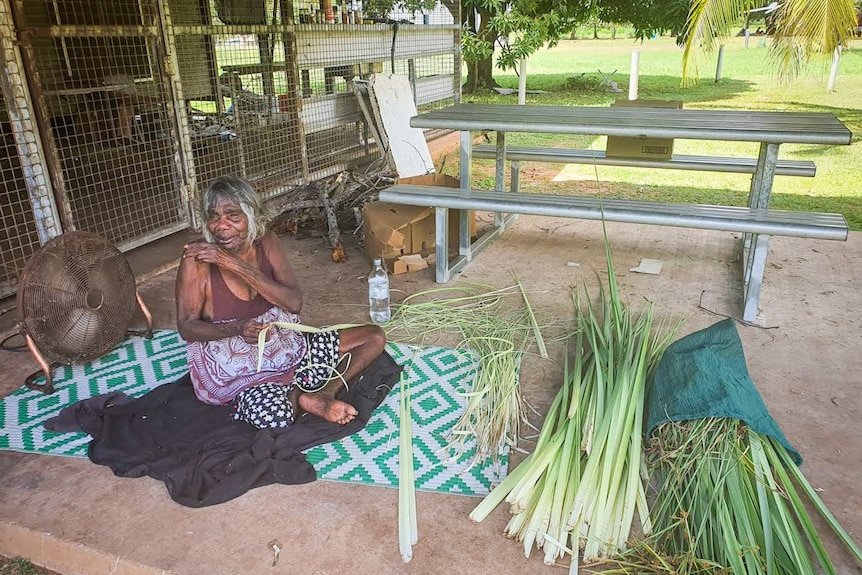 Mary Dadbalag sitting on a mat with a pile of pandanus leaves weaving.