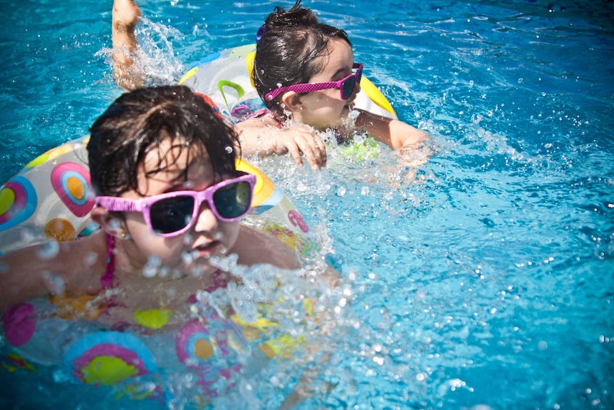 Two young kids wearing sunglasses floating in a swimming pool on pool toys