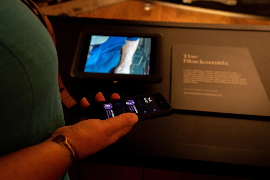 A close-up shot of a hand holding an iPod Touch in front of a small iPad screen in a museum.