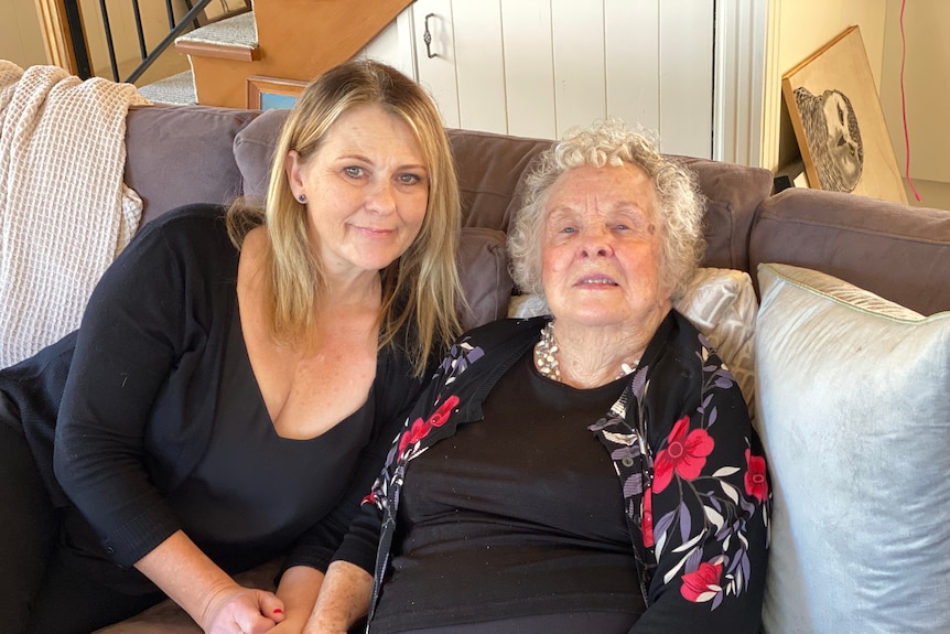 A young woman and an older woman who are friends sit next to each other on couch.