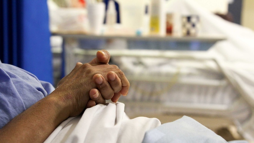 Close-up of an elderly person's hands in a hospital bed.