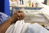 A patient in hospital folds their hands and rests them on the bed covers