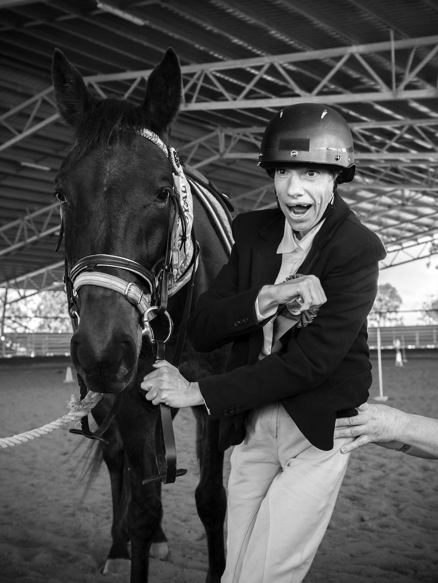 A black and white photographs of a lady standing next to a horse