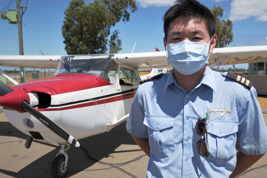 A pilot wearing a white face mask standing next to a red and white light aircraft.
