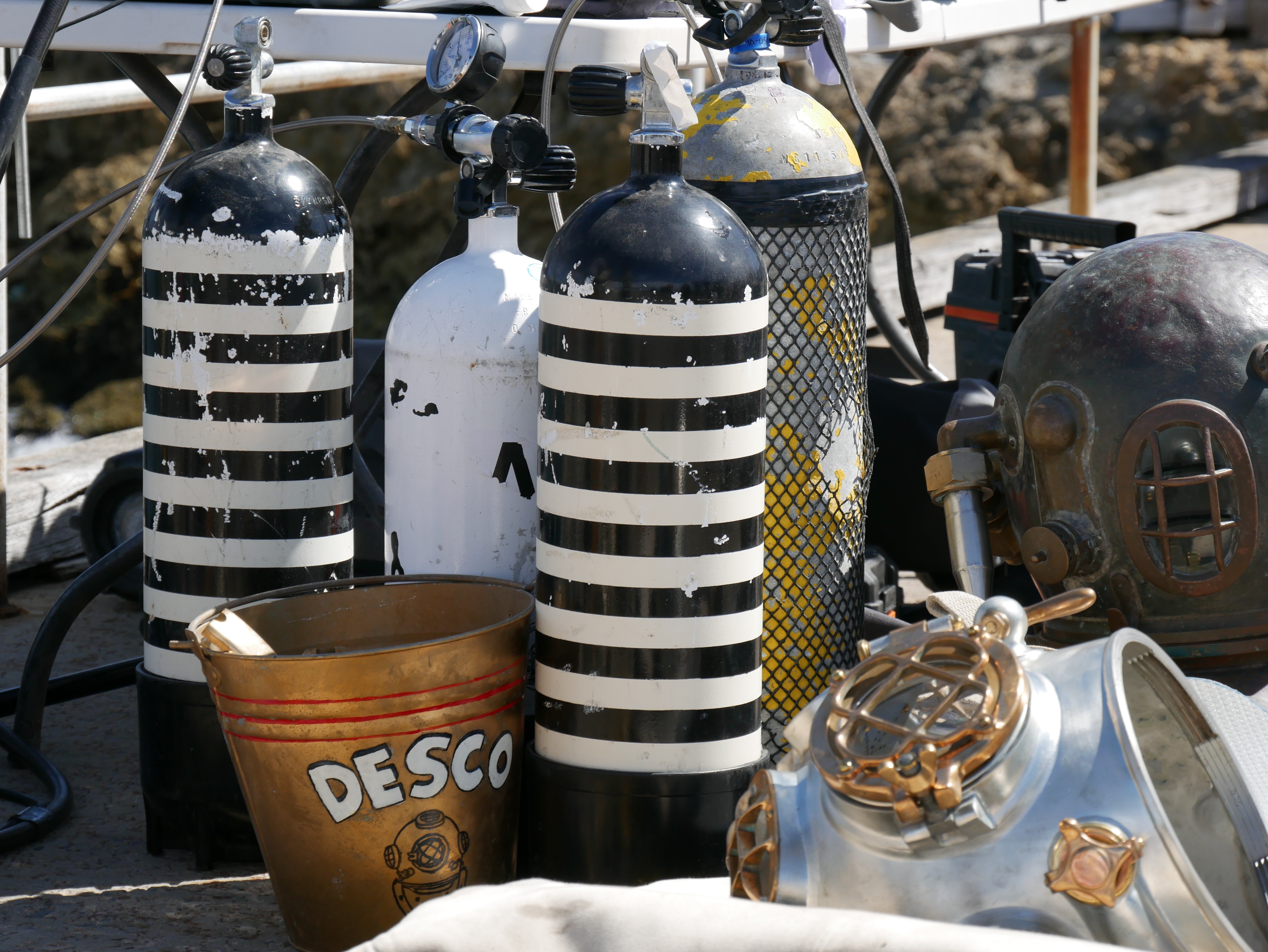 Old black and white striped oxygen tanks stand next to a metal bucket painted with the letters DESCO. 