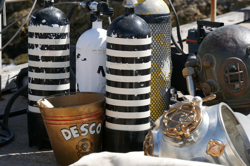 Old black and white striped oxygen tanks stand next to a metal bucket painted with the letters DESCO. 