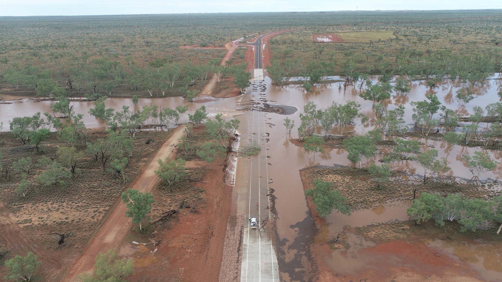 Um carro com trabalhadores de alta visibilidade parou nas margens de um rio enquanto derrubava árvores e cobria a estrada.