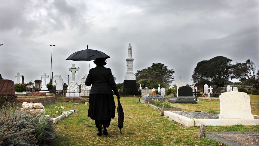 A woman dressed in black among gravestones in a cemetery