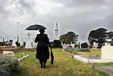 A woman dressed in black among gravestones in a cemetery