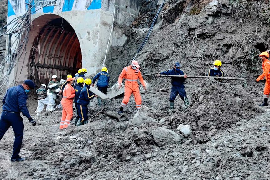 Workers in yellow, blue overalls move debris near tunnel