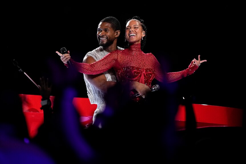 Usher in a white jewelled vest standing behind Alicia Keys, sparkly red long sleeved bodysuit 