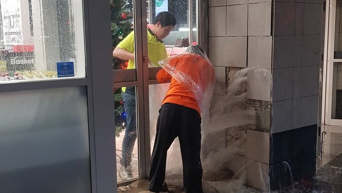 Water pours out of a wall at a Woolworths near Town Hall Station in Sydney's CBD as workers fight to stop it.