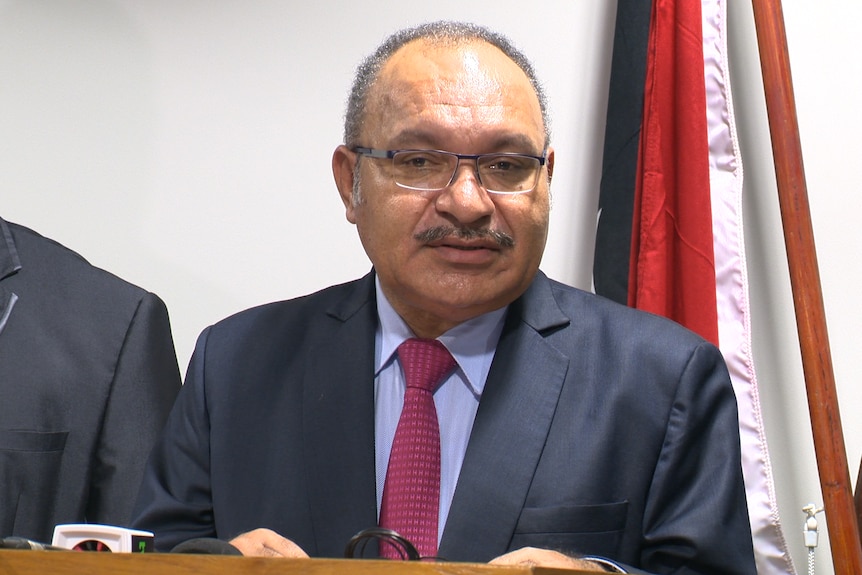 Peter O'Neill talks in front of a PNG flag at a press conference.