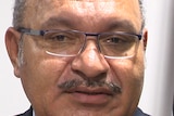 Peter O'Neill talks in front of a PNG flag at a press conference.