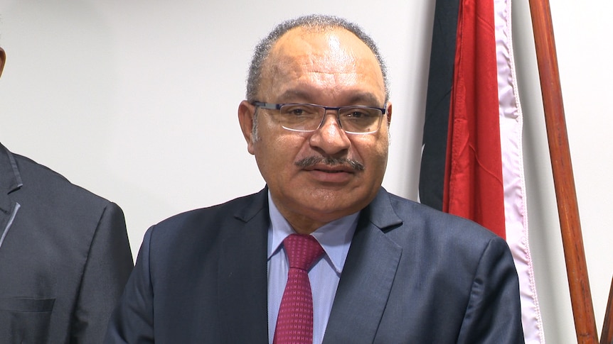 Peter O'Neill talks in front of a PNG flag at a press conference.