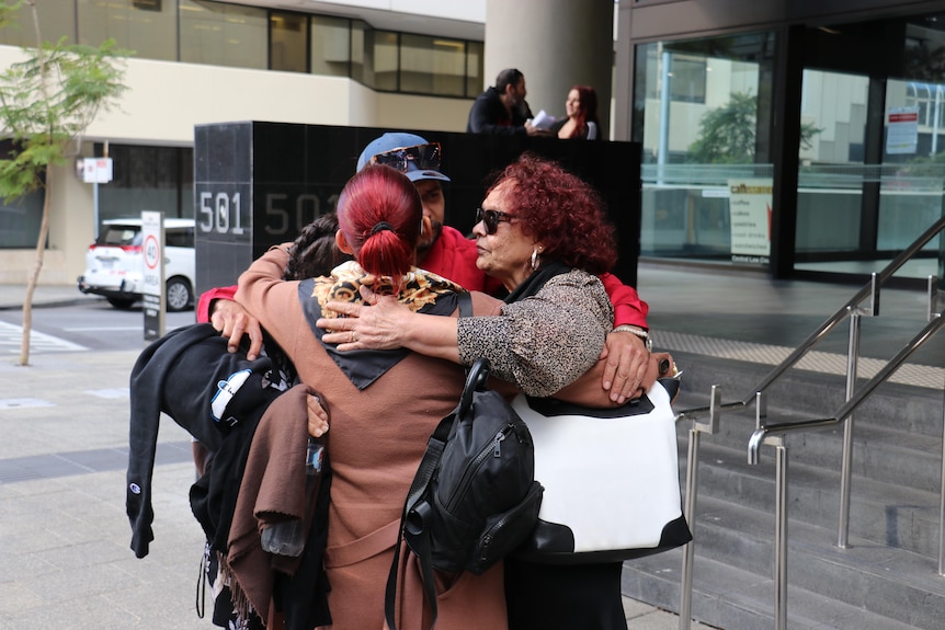 A group of people hugging outside a court building.