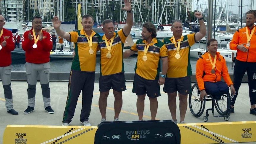 Four men in yellow and green shirts stand celebrating with gold medals around their necks.