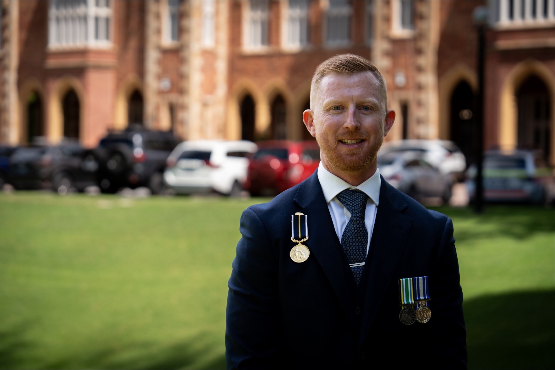 Carl Pilkington poses for a photo smiling outside WA Government House wearing a number of medals on his jacket.