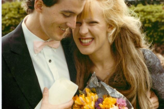 A photo of a man smiling with a woman holding flowers close to her