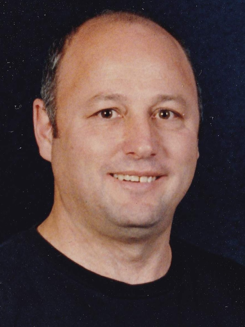 A portrait shot of a middle-aged man, smiling, against a black background