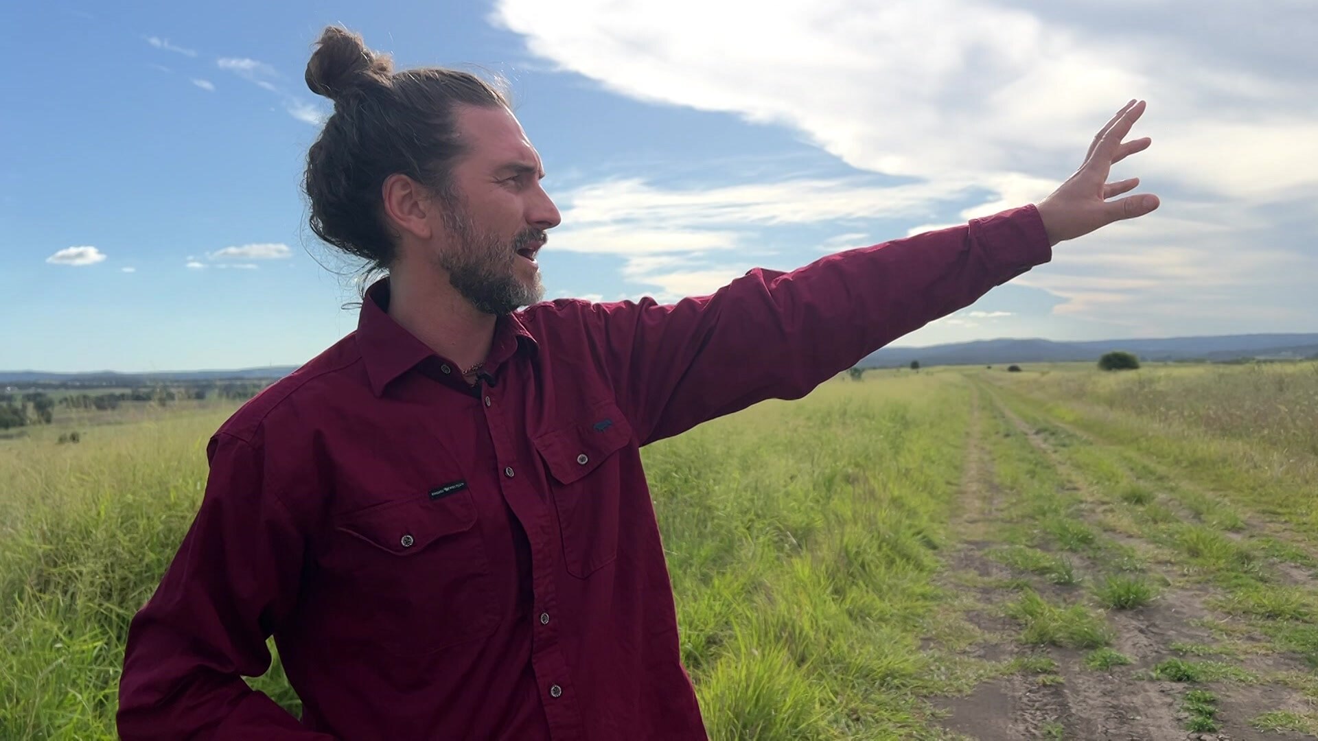 A man in a red shirt with his hand outstretched in a field