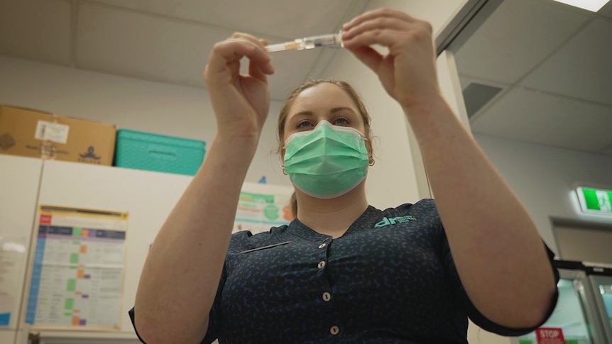 A nurse in a mask looks at a flu vaccination.