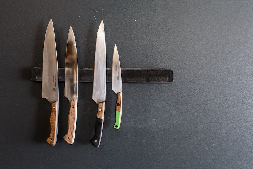 A charcoal grey wall with four knives mounted on a metal strip.