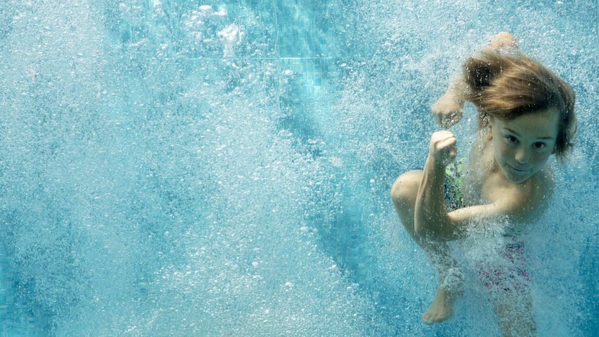 A young boy underwater in a pool, looking at the camera.