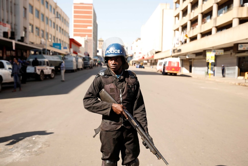 A police officer with a gun stands guard in the middle of a street in Harare.