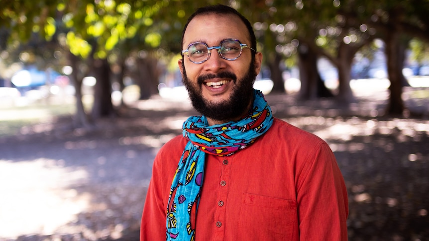 An image of Jonathan Sriranganathan wearing red clothing and a scarf with trees in the background.