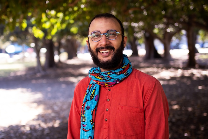 An image of Jonathan Sriranganathan wearing red clothing and a scarf with trees in the background.