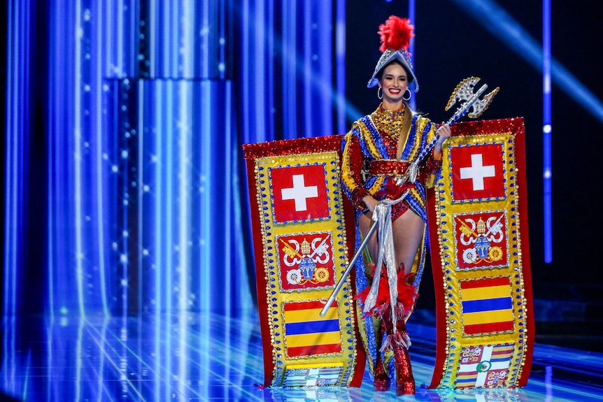 Lorena Santen wearing a glittery knight's helmet, a yellow-and-blue leotard and holding a glittery axe
